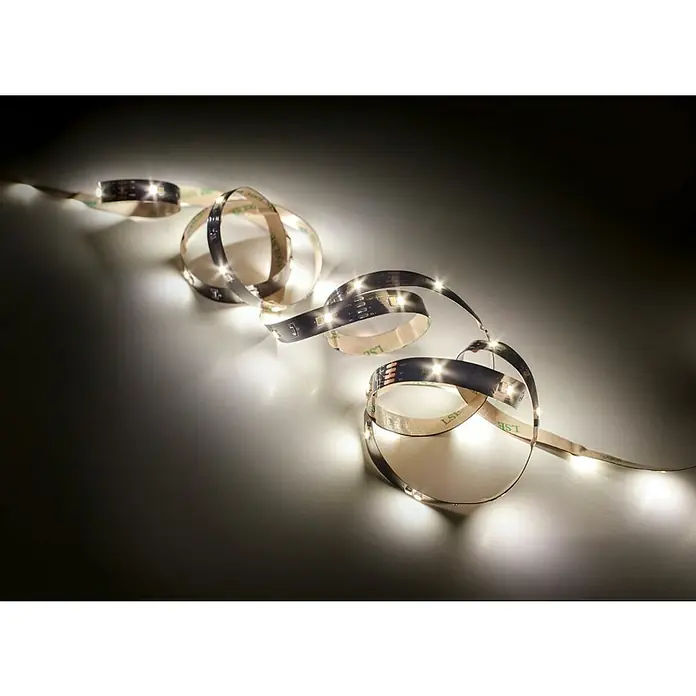 Trio Lighting Tira LED Chip - Largo: 3 m, Blanco frío - Tira de LED: Primer plano de una tira de luz LED flexible dispuesta artísticamente sobre una superficie, emitiendo un brillo cálido y acogedor.
