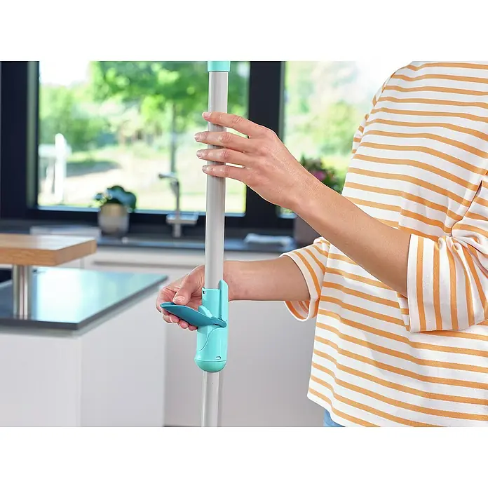 Leifheit Bodenwisch-Set Clean Twist M Ergo - 4 -tlg., 6 l - Nahaufnahme eines Moppstiels mit türkisfarbenem Clip in einer modernen Küche, gehalten von einer Person im gestreiften Oberteil.