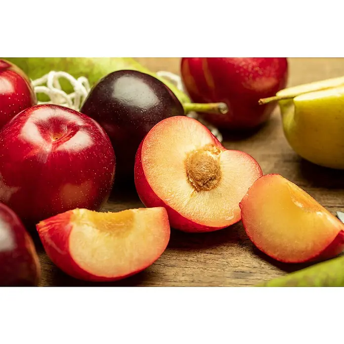 Piardino Pfirsich - Prunus persica 'Crimson Gold', Erntezeit: August - Nahaufnahme von Pflaumen, die auf einem Holztisch liegen, einige sind ganz, andere aufgeschnitten, um das Fruchtfleisch zu zeigen.