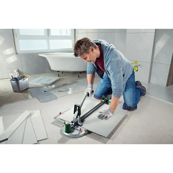 Bosch Fliesenschneider PTC 640 - Max. Schnittlänge: 640 mm - Ein Mann kniet und schneidet eine Fliese mit einem Fliesenschneider. Die Fliese liegt auf einer grünen Schneideunterlage.