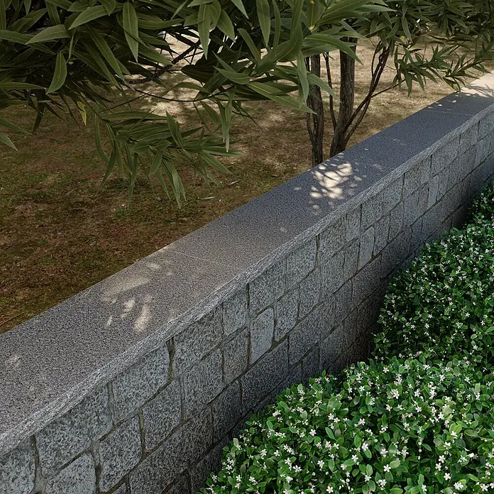 Mauerabdeckplatte G 654 - Anthrazit, 100 x 32 x 4 cm - Diese Aufnahme zeigt eine graue Steinmauer, die eine friedliche Gartenszene mit üppigem Grün und Bäumen einrahmt.