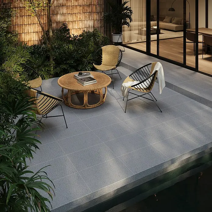 Terrassenplatte G654 - 60 x 40 x 3 cm, Anthrazit, Granit - Eine stilvolle Gartensitzgruppe mit Rattansesseln und Tisch auf einer grauen Steinterrasse, umgeben von üppigem Grün.