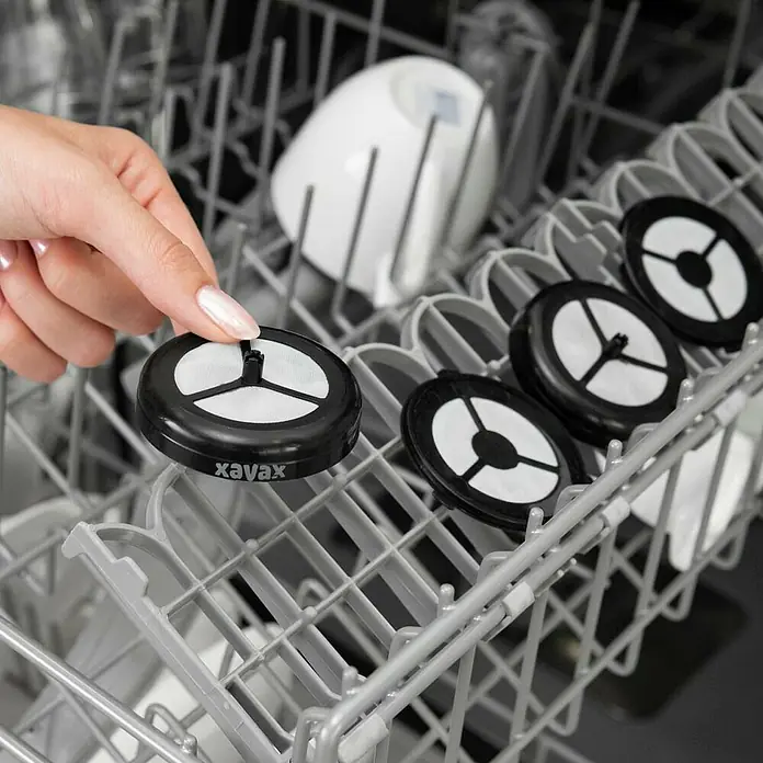 Xavax Kaffeepad - 2 Stk. - Eine Hand platziert einen schwarzen xavax Geschirrspülerfilter mit weißem Sieb in einem Geschirrkorb.