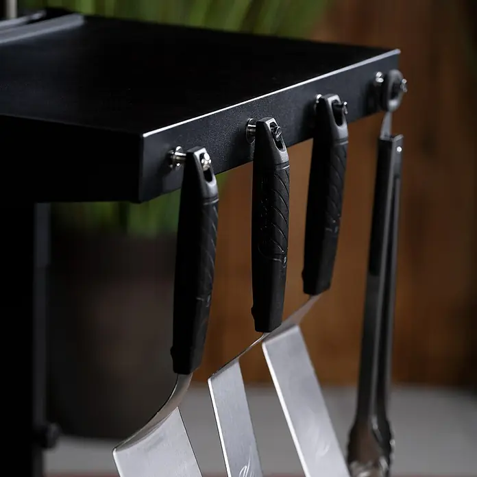 Blackstone Plancha-Grill 36" mit Airfryer - Grillfläche (B x T): 91 x 55 cm, 17,5 kW, Schwarz - Detailaufnahme eines Grilltisches mit Zubehör, darunter Wender und Zangen, die an Haken hängen. Fokus auf Ordnung am Grill.