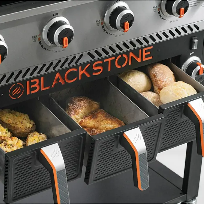 Blackstone Plancha-Grill 36" mit Airfryer - Grillfläche (B x T): 91 x 55 cm, 17,5 kW, Schwarz - Nahaufnahme des Blackstone Grills mit ausziehbaren Warmhalteschubladen, gefüllt mit verschiedenen Speisen, perfekt für BBQ-Enthusiasten.