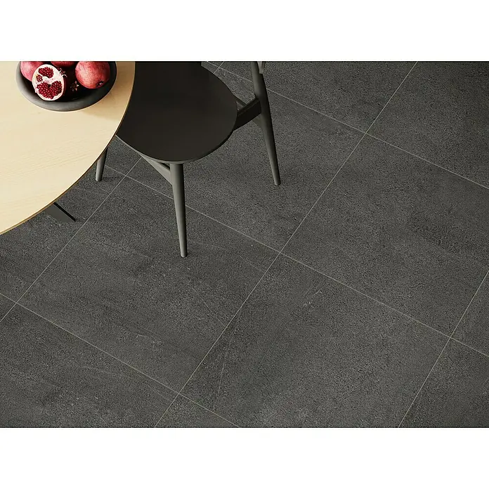 Terrassenfliese Patio - 60 x 60 x 2 cm, Anthrazit, Matt - Nahaufnahme eines dunklen Keramikfliesenbodens mit einem Stuhl und einem Tisch mit Früchten, der die Textur und das Design der Fliesen hervorhebt.