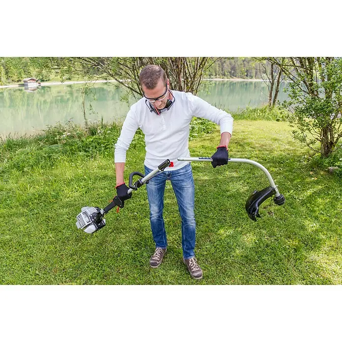 AL-KO Benzin-Motorsense BC 223 L-S - 700 W, Schnittbreite Faden: 41 cm - Ein Mann bedient eine Benzin-betriebene Motorsense im Freien, umgeben von grüner Natur und einem See. Er trägt Schutzausrüstung.