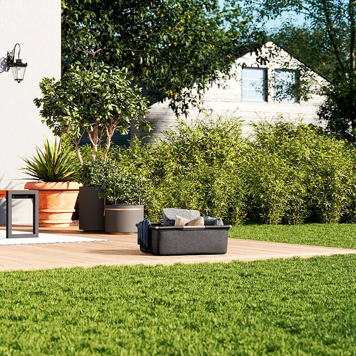 Sunfun Lumar Korb für Kissenbox - L x B x H: 66,5 x 54,5 x 25 cm, Night-Grey - Eine stilvolle, graue Aufbewahrungsbox für den Außenbereich mit Textilien auf einer Holzterrasse, umgeben von üppigem Grün und einem Haus im Hintergrund.