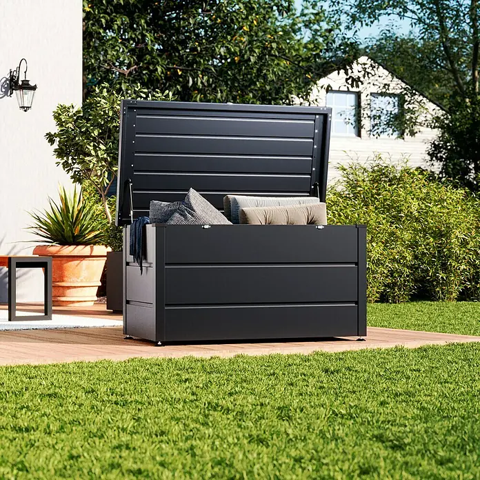 Hörmann EcoStar Gartenbox Elegant136 x 67,2 x 72,5 cm, Anthrazit, Stahl - Bild eines modernen, schwarzen Gartenkoffers mit geöffnetem Deckel, der Kissen enthält, auf einer Holzterrasse inmitten eines Gartens.