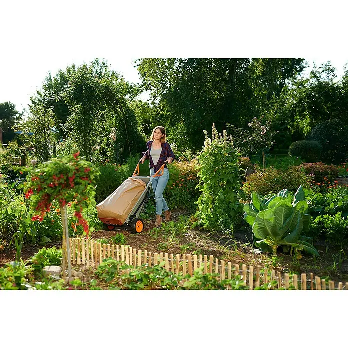 Worx Schubkarre Aerocart Multifunktion 8-in-175 l, Stahl, Traglast: 136 kg - Eine Frau zieht einen Gartentrolley mit Gartensack durch einen üppigen Garten, umgeben von üppigem Grün und Blumen.