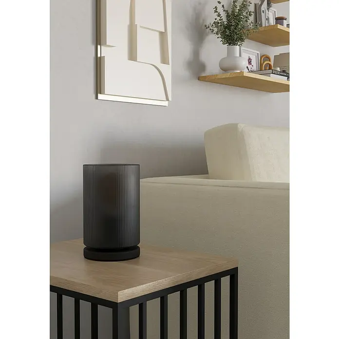 Eglo LED-Tischleuchte Colomera - 40 W, Schwarz, Ø x H: 12 x 19,5 cm - Eine dunkelgraue, gerippte zylindrische Ambientelampe steht auf einem Beistelltisch neben einem hellen Sofa.
