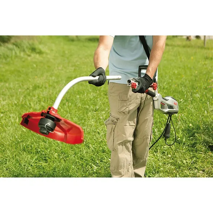 AL-KO Elektro-Rasentrimmer BC 1000 E - 1.000 W, Schnittbreite Faden: 35 cm - Ein Mann benutzt einen AL-KO Rasentrimmer im Garten, um das Gras zu trimmen. Das Gerät ist rot und silber, mit einem Tragegurt.
