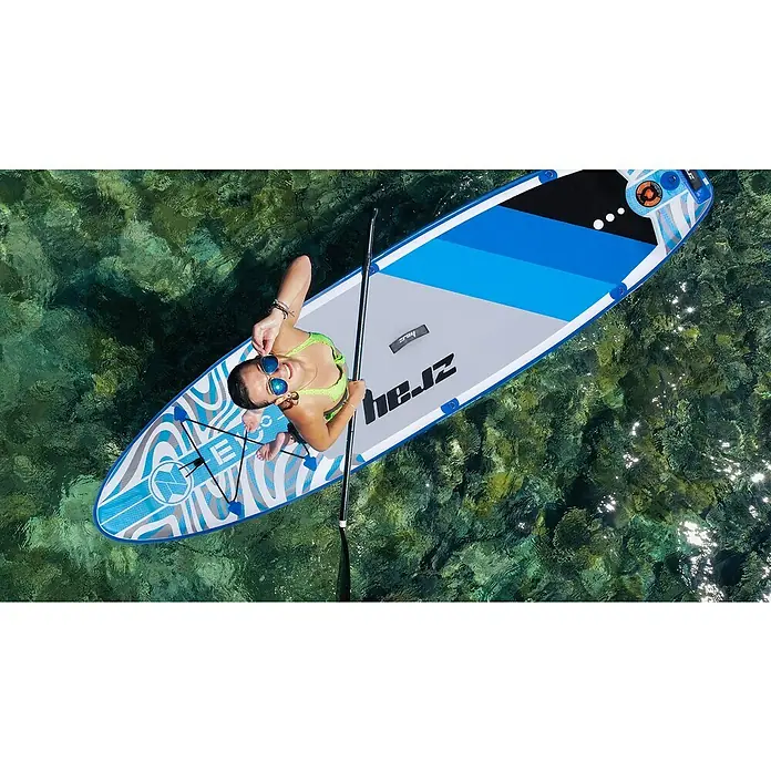 SUP-Board-Set ZRay E10 - L x B x H: 297 x 76 x 13 cm, Nutzlast: 110 kg, Aufblasbar - Frau auf einem aufblasbaren Paddleboard der Marke Herz im Meer. Das Board hat ein blau-graues Design und ist für Wassersport konzipiert.