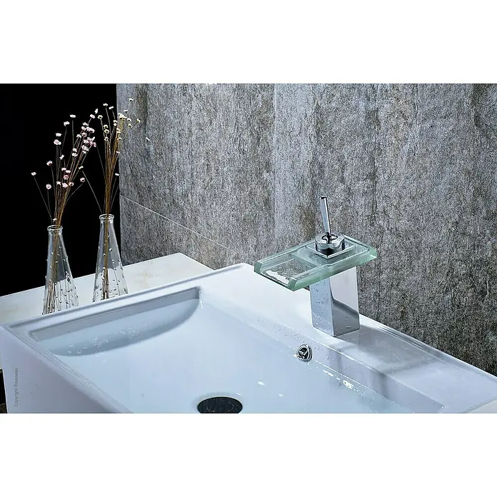 Rousseau Cristali Grifo de lavabo cascada - Cromo, Brillante - Lavabo de baño moderno con un elegante grifo de vidrio y cromo, complementado con decoraciones elegantes y una pared gris texturizada.