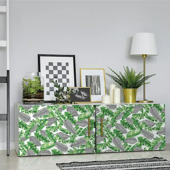 D-c-fix Rollo adhesivo vinílico Botánico Uva - 200 x 45 cm, Verde, Autoadhesivo - Una cómoda con un estampado de hojas tropicales, adornada con marcos de fotos, plantas y velas, aportando un toque fresco y natural a cualquier habitación.