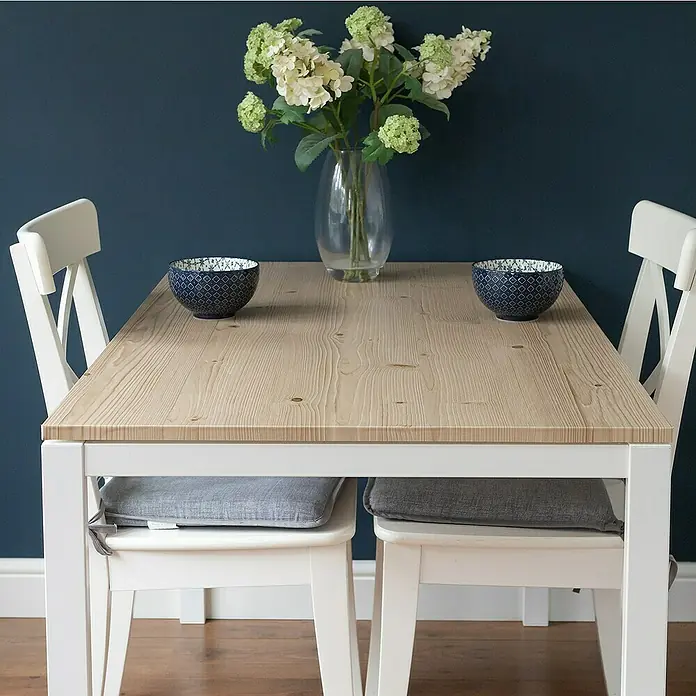 D-c-fix Rollo adhesivo vinílico Jura - 200 x 45 cm, Marrón, Autoadhesivo - Una mesa de comedor con tablero de madera, patas blancas, sillas con cojines grises y un jarrón de flores.