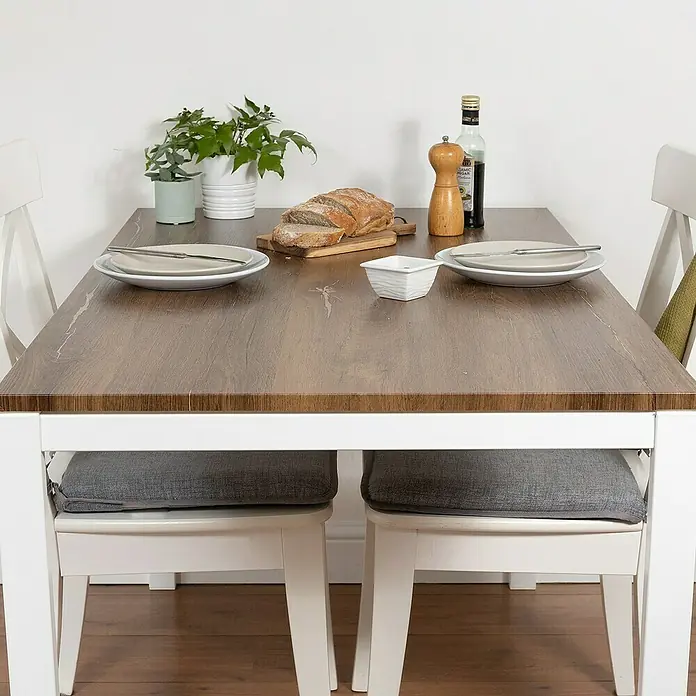 D-c-fix Rollo adhesivo vinílico Roble Asta - 200 x 45 cm, Roble, Autoadhesivo - Primer plano de una mesa de comedor con tablero de madera y sillas blancas, adornada con platos, pan, plantas y condimentos.