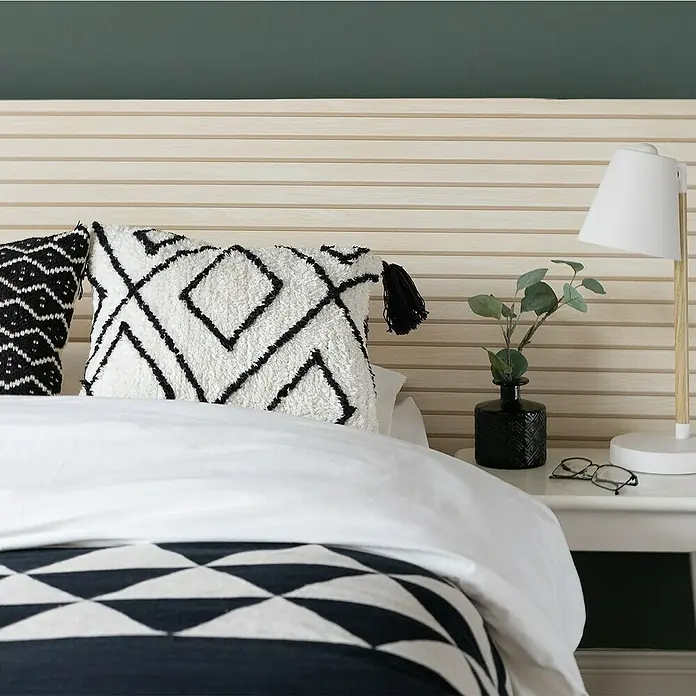 D-c-fix Rollo adhesivo vinílico Listones de madera - 200 x 45 cm, Marrón, Autoadhesivo - Un dormitorio acogedor con una cama elegante con cojines geométricos y una manta decorativa. Lámpara y gafas colocadas en la mesita de noche.