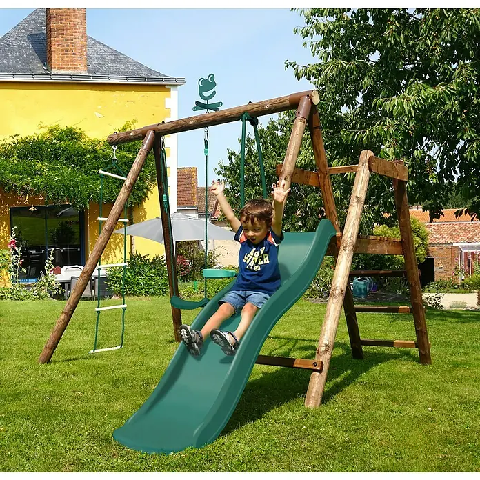 Soulet Schaukel Murier - B x L: 283 x 243 cm, Holz - Ein Kind saust die grüne Rutsche des hölzernen Spielturms im Garten hinunter.