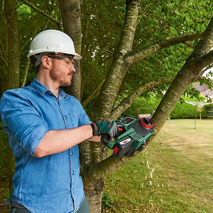 Bosch Power for All 18V Akku-Kettensäge UniversalChain 18 - 18 V, Li-Ionen, 1 Akku, Schwertlänge: 20 cm - Ein Mann mit Helm schneidet einen Ast mit einer Bosch Akku-Kettensäge. Ideal für Baumschnittarbeiten im Garten.