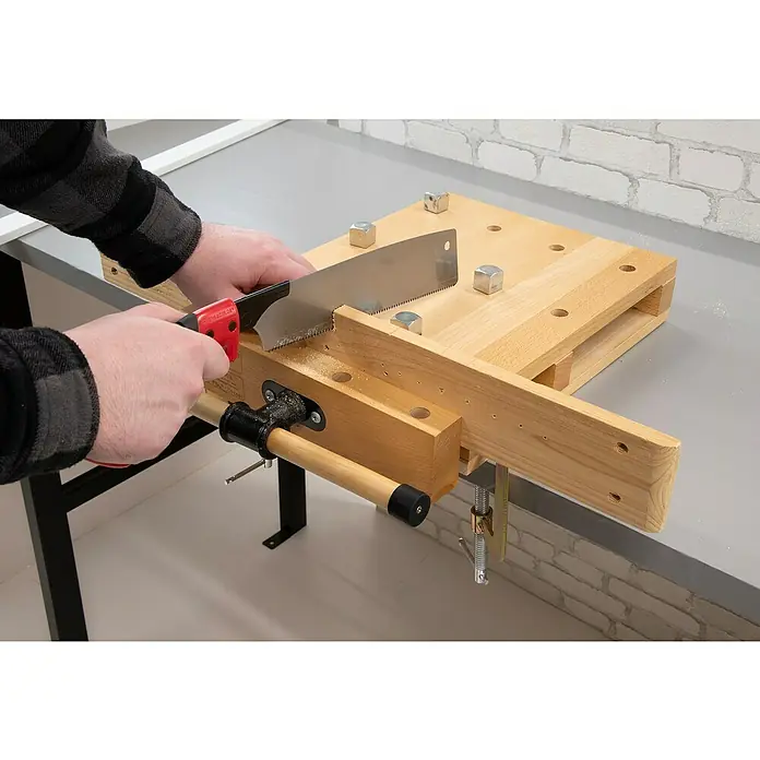 Rikta Hobelbank - L x B: 47 x 29 cm, Arbeitshöhe: 7 cm, Holz - Nahaufnahme einer Person, die mit einer Handsäge ein Holzstück auf einer Werkbank sägt, wobei die Holzbearbeitung im Fokus steht.
