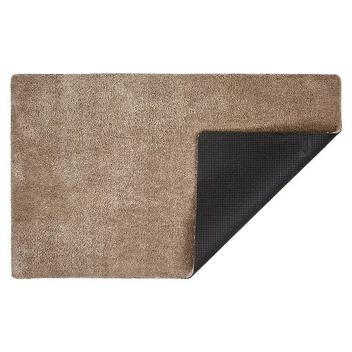 Fußmatte Moon - Taupe, 100 x 60 cm, 100 % Polyester - Dieser Teppich hat eine braune Floroberfläche und eine schwarze, rutschfeste Unterseite. Er ist rechteckig und leicht angehoben an einer Ecke.