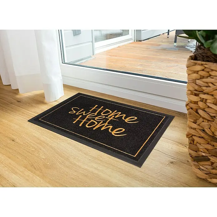 Astra Homelike Fußmatte Home Sweet Home - Schwarz/Gold, 40 x 60 cm, 100 % Polyamid - Die Fußmatte "Home Sweet Home" in Schwarz und Gold liegt vor einer Terrassentür auf einem hellen Holzboden. Ein dekorativer Willkommensgruß!