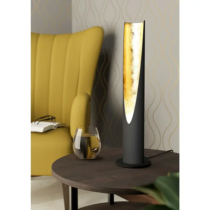 Eglo Barbotto LED-Tischleuchte rund - 5 W, Ø x H: 100 mm x 39,5 cm, Gold, Schwarz, Warmweiß - Eine Nahaufnahme einer modernen Tischleuchte mit goldenem Akzent auf einem dunklen Holztisch neben einem gelben Sessel.