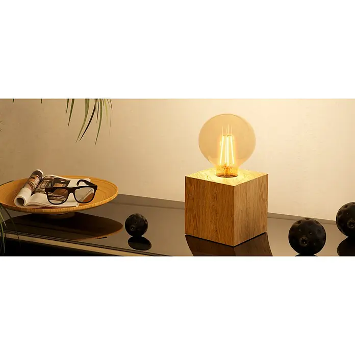 Eglo Tischleuchte PRESTWICK 2 - 40 W, L x B x H: 9,5 x 9,5 x 9,5 cm, Braun, E27 - Würfelförmige Tischlampe aus Holz mit glühender Edison-Glühbirne, auf dunkler, spiegelnder Fläche neben Magazin und Sonnenbrille.