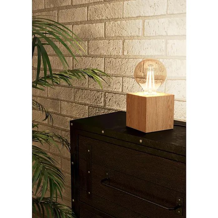 Eglo Tischleuchte PRESTWICK 2 - 40 W, L x B x H: 9,5 x 9,5 x 9,5 cm, Braun, E27 - Eine warme Holzblocklampe mit einer leuchtenden Edison-Glühbirne steht auf einer dunklen Kommode und beleuchtet eine Ziegelwand.