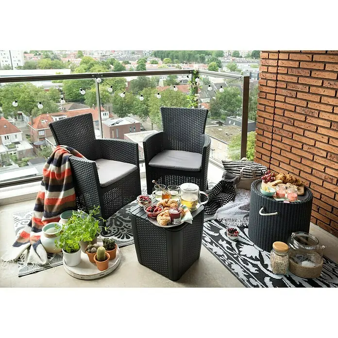 Keter Conjunto de muebles de balcón Iowa - 3 pzs., Antracita - Acogedora escena de balcón con sillones de ratán negro y mesas auxiliares, decorada con plantas, mantas y un juego de desayuno.
