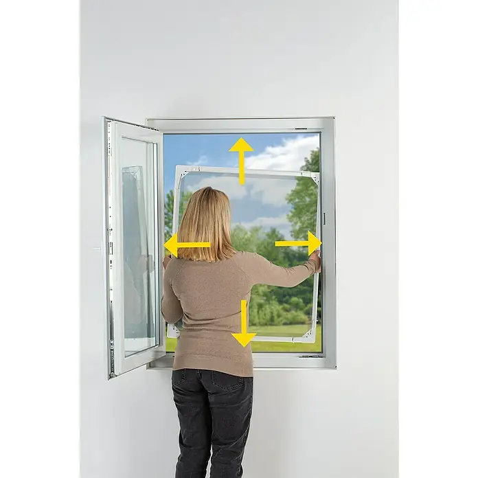Easy Maxx Insektenschutzfenster - B x H: 115 x 135 cm, Montage Insektengitter: Klemmen, Farbe Rahmen: Weiß - Eine Frau installiert einen Insektenschutzrahmen in ein Fenster. Der Rahmen ist weiß und die Frau trägt ein beiges Oberteil und dunkle Jeans.