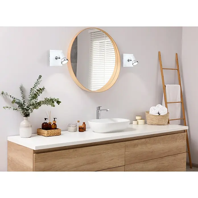 Eglo LED-Wandstrahler Tamara 1 - 3 W, Chrom, Weiß - Ein modernes Badezimmer-Interieur mit einem runden Spiegel, zwei Wandleuchten, einem Waschbecken und einer Holzkommode.
