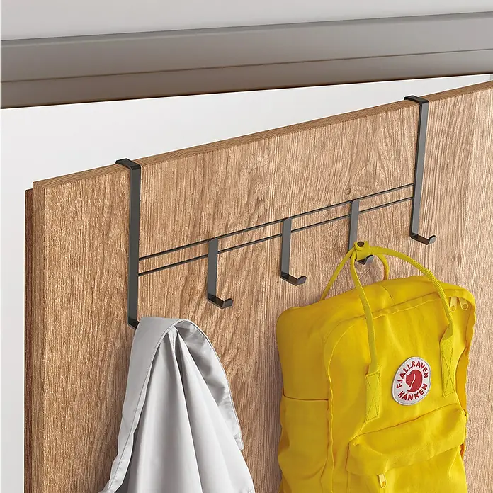Metaltex Türhaken - Lavaschwarz, L x B x H: 4,5 x 38 x 15 cm, Anzahl Haken: 5 Stk., Metall - Das Bild zeigt eine Türgarderobe mit Haken, an der eine Jacke und ein Rucksack hängen. Die Garderobe ist aus Metall und wird über die Tür gehängt.