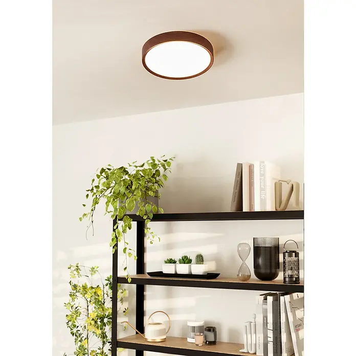 Eglo LED-Deckenleuchte rund MUSURITA - 19,5 W, Ø x H: 340 mm x 6 cm, Holz, Warmweiß - Diese Nahaufnahme zeigt eine moderne Deckenleuchte mit Holzrand an einer weißen Decke über einem Regal mit verschiedenen Dekorationen.