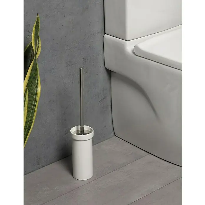 Tatay Slim Escobillero de suelo - Blanco/Cromo - Un portaescobillas de baño blanco con escobilla de acero inoxidable junto a un inodoro y una planta de interior. Accesorios de baño.