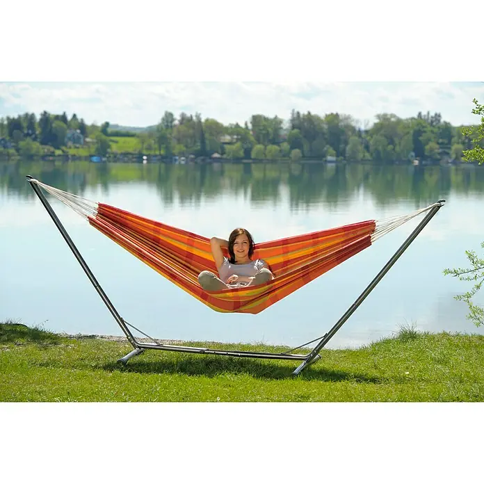 Amazonas Hängemattengestell Suma Grande - L x B x H: 320 x 107 x 132 cm, Metall - Frau entspannt in einer bunten Hängematte mit Gestell am See und genießt die Ruhe.
