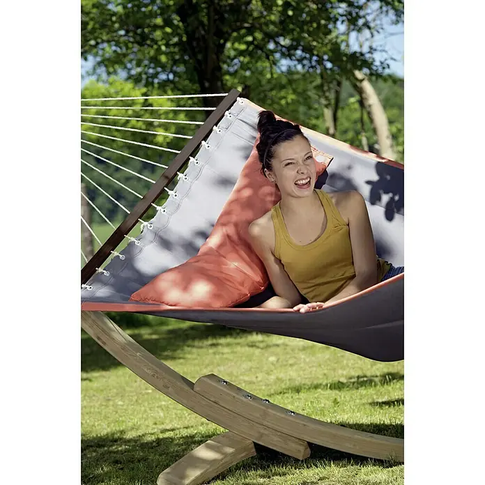 Amazonas Stabhängematte American Dream - L x B: 335 x 120 cm, Grau - Eine junge Frau entspannt in einer Hängematte mit Holzrahmen und grauer Liegefläche, inklusive Kissen, im Garten.