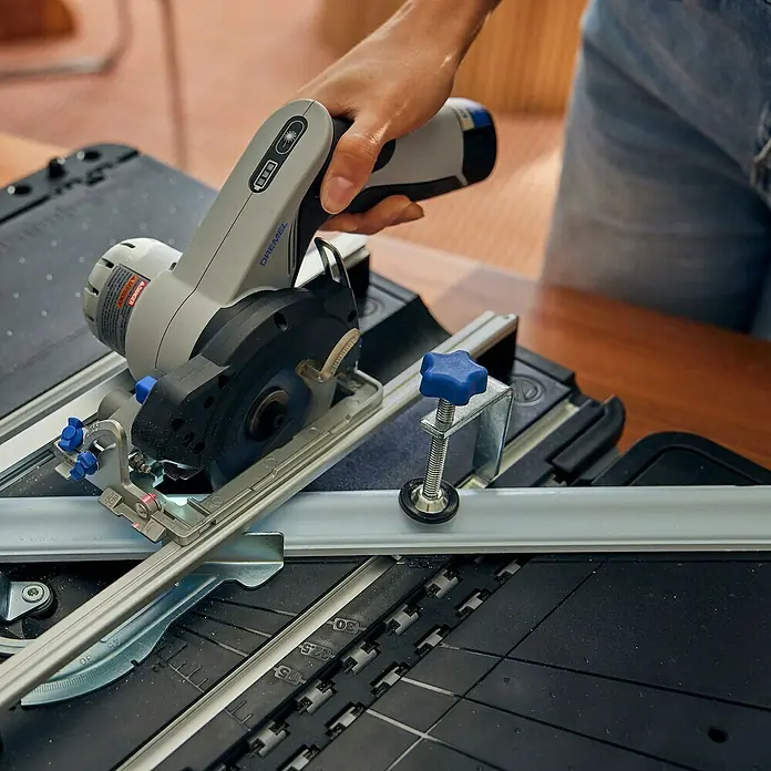 Dremel Mobile Sägestation Blueprint CS12V-S1C - 12 V, 1 Akku, 2 Ah, Leerlaufdrehzahl: 5.000 U/min - Eine Dremel Kreissäge schneidet präzise ein Werkstück auf einer schwarzen Werkbank mit Führungsschiene.