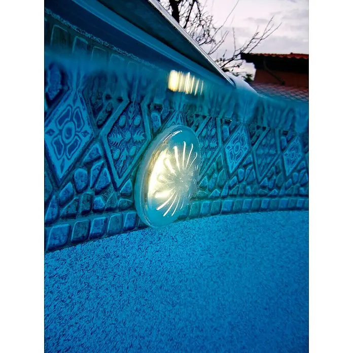 Gre Luz LED para piscinas Proyector - Blanco, LED - Primer plano de una pared de piscina con una luz redonda empotrada, que irradia un brillo cálido que acentúa el tono azul.