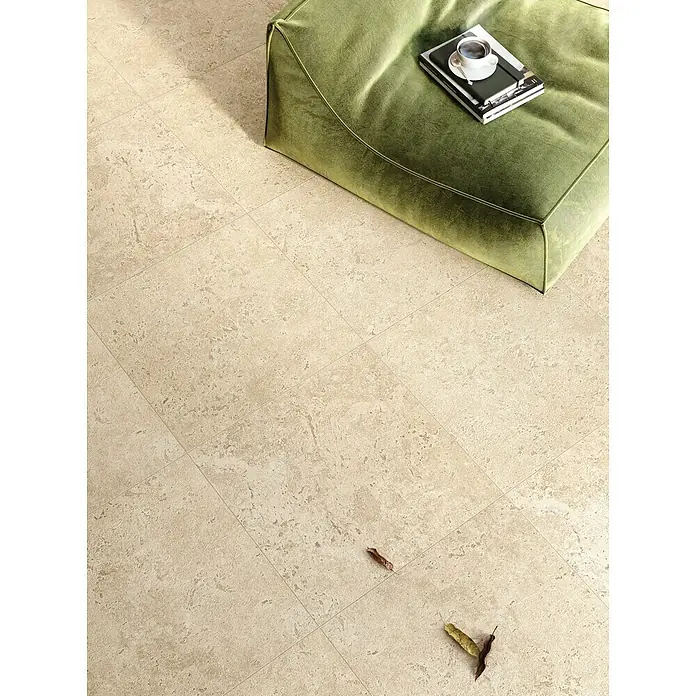 Corso Italia Terrassenfliese Pompei Aureo Crosscut - 60 x 60 cm, Beige, Matt - Ein grüner Sitzhocker mit Buch und Tasse darauf steht auf einem beigen Fliesenboden. Natürliche Elemente wie Blätter verzieren den Boden.