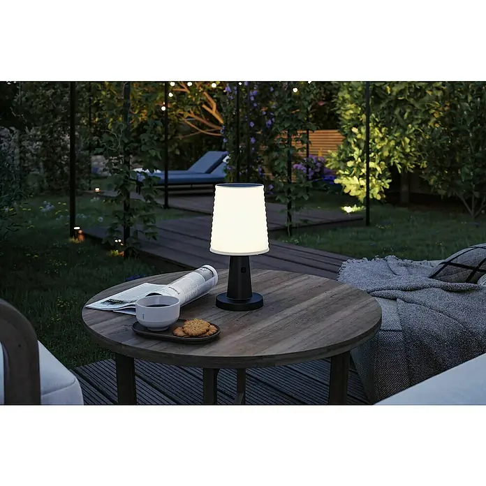 Paulmann Solar-Tischleuchte Ilanga - 32 W, Weiß/ Anthrazit, IP44 - Eine beleuchtete weiße und schwarze tragbare Tischlampe steht nachts auf einem Holztisch im Garten.