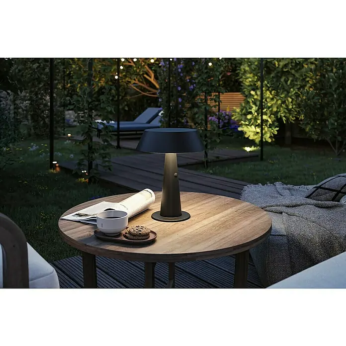 Paulmann Solar-Tischleuchte Soala - 32 W, Schwarz, IP44 - Dunkelgraue tragbare Tischlampe beleuchtet einen Holztisch im Garten bei Nacht, auf dem Kaffee und Kekse stehen.