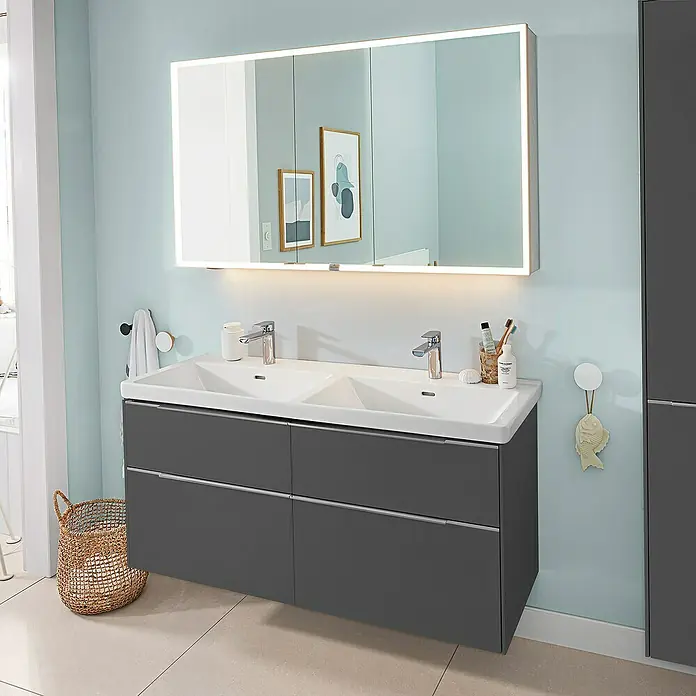 Villeroy & Boch Subway 3.0 Waschbeckenunterschrank - Graphite, Anzahl Schubladen: 4 Stk., Farbe Griff: Aluminium glänzend, B x T x H: 127,2 x 47,8 x 57,6 cm, Mit Beleuchtung, Geeignet für Doppelwaschtisch - Moderner Doppelwaschtisch mit dunkelgrauem Unterschrank, weißen Becken und beleuchtetem Spiegelschrank in hellblauem Bad.