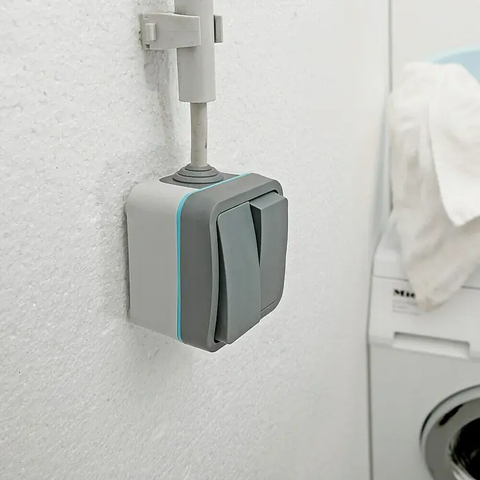Voltomat Blueline Feuchtraum-Serienschalter - Grau, Aufputzmontage, IP54 - Nahaufnahme eines grauen Doppel-Lichtschalters mit blauen Akzenten, der an einer weißen Wand montiert ist.