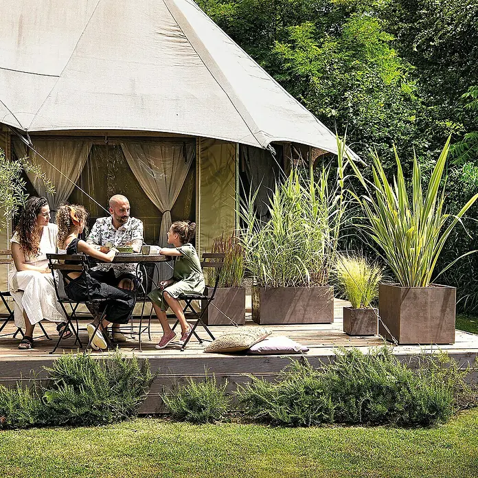 Deroma Millennium Maceta para planta - 39 x 39 x 39 cm, Plástico, Brownstone - Familia disfrutando de un tiempo al aire libre en una terraza de madera con jardineras elegantes que mejoran la experiencia de glamping.