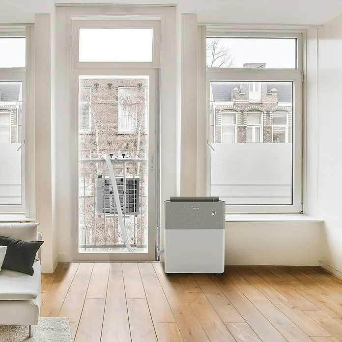 Midea Klimasplitgerät PortaSplit Cool 8.000 Btu - Kühlleistung: 2.300 W, Raumgröße: 28 m² - Midea mobiles Klimagerät, weiß und grau, mit Außeneinheit auf Balkongeländer und durch eine Tür mit der Inneneinheit verbunden.