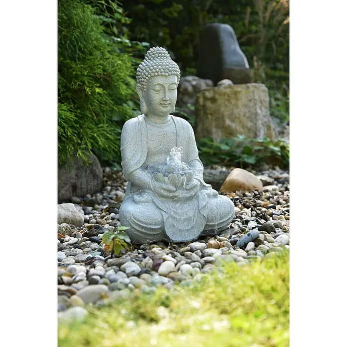 Heissner Wasserspeier Tempelfigur - L x B x H: 240 x 310 x 480 mm - Graue Buddha-Brunnenfigur in Steinoptik mit Wasser, das aus einem Lotus in einer Gartenumgebung fließt.