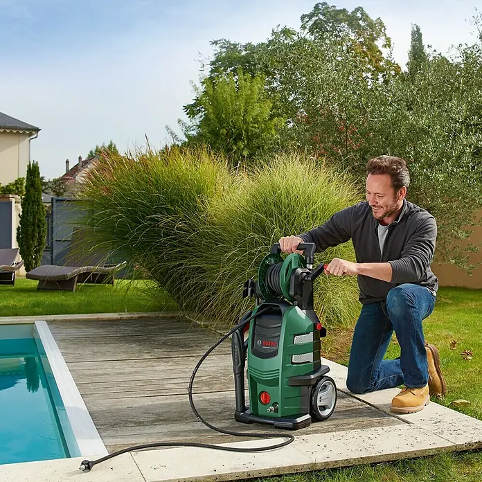 Bosch Hochdruckreiniger AdvancedAquatak 160 - 2.600 W, Max. Druck: 160 bar, Fördermenge: 570 l/h - Ein Mann bedient einen grünen Bosch Hochdruckreiniger mit Schlauchtrommel neben einem Pool.