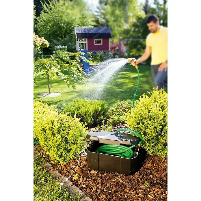 Heissner Garten-Aufbewahrungsbox - L x B x H: 40 x 30 x 21 cm, Kunststoff - Schwarze Schlauchbox mit grünem Schlauch, offen im Garten, Mann bewässert Pflanzen.
